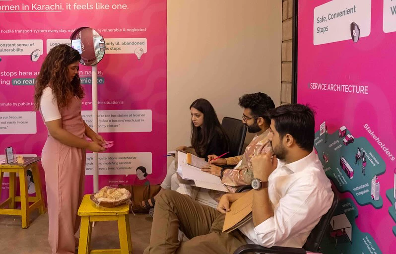 Nabia presenting SafeHer at the IVS Degree Show, with three visitors taking notes in front of the SafeHer panels